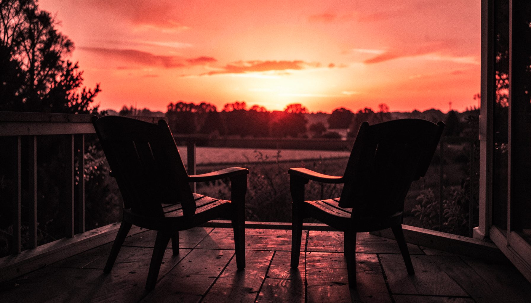 Two chairs on a porch facing a sunset, quiet conversation setting, warm golden hour light