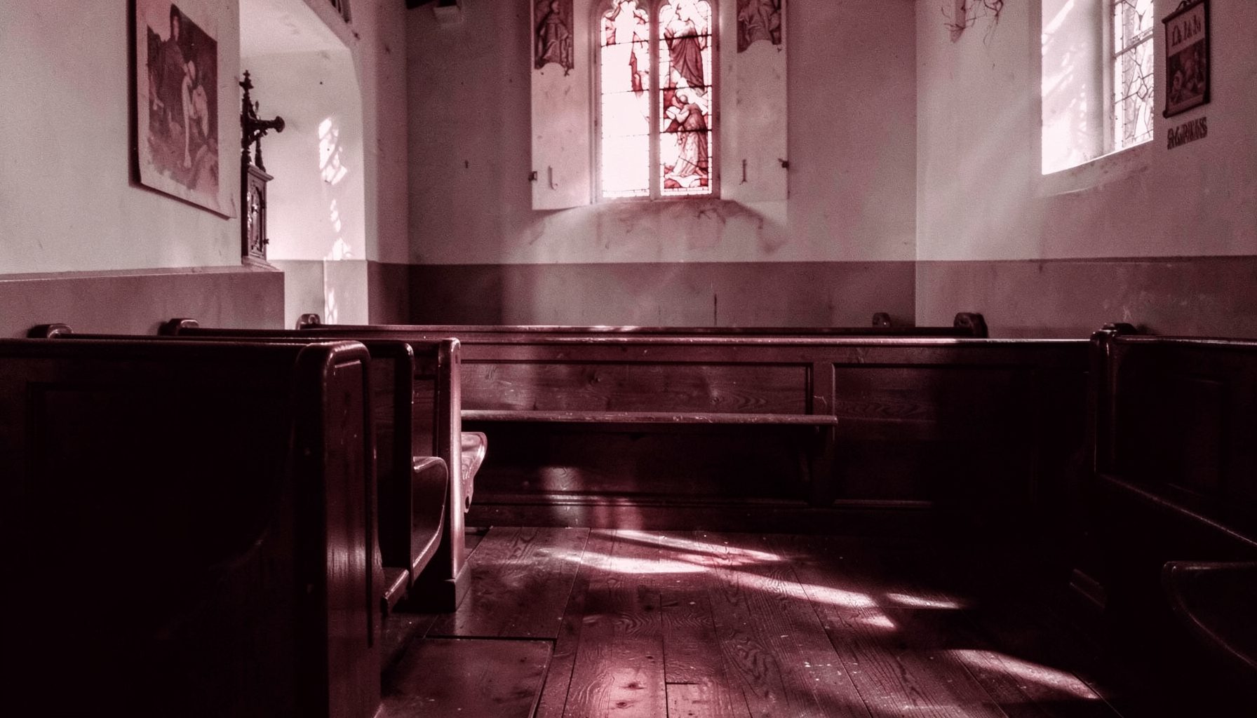 A church pew in soft afternoon light, quiet and empty, with stained-glass reflections on wood