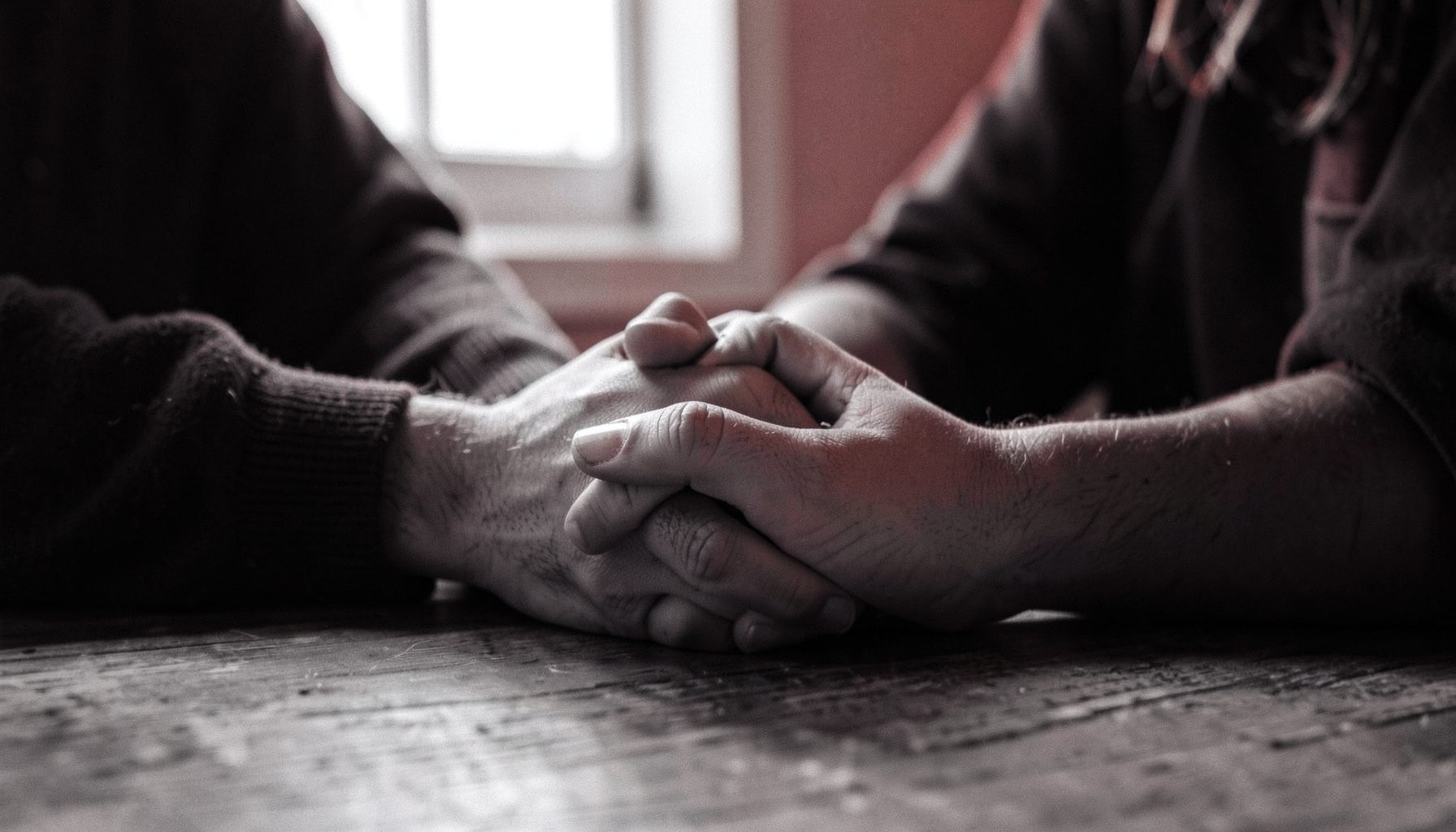 A couple's hands intertwined on a wooden table, soft window light, intimate and warm